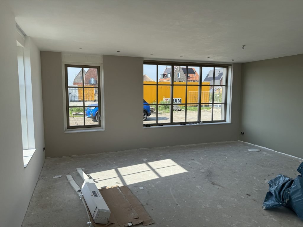 Grote nieuwbouwkamer met wanden in een warme grijstint en twee brede raampartijen